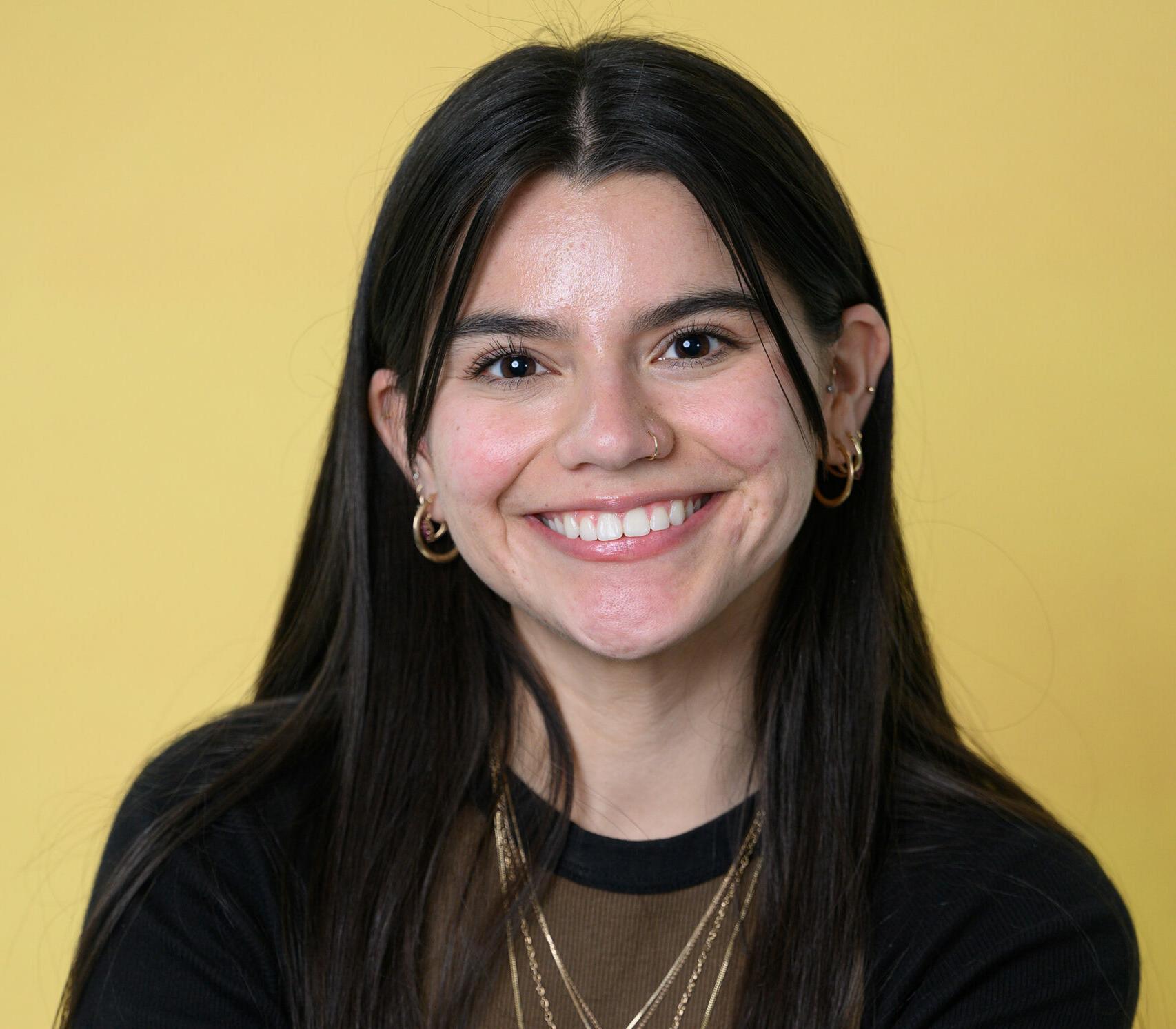 A female student is smiling in front of a yellow background