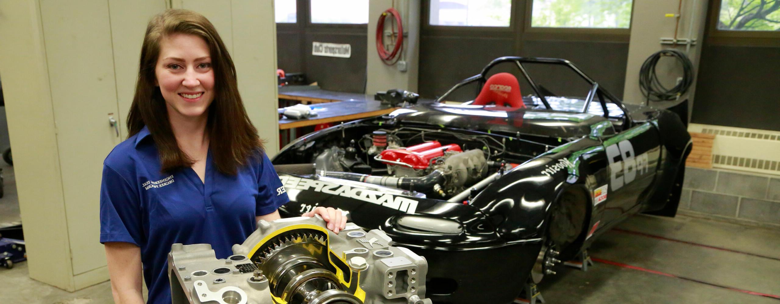 female in blue shirt and race car with hood off exposing engine